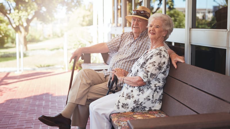 Retired couple sitting on a bench outside their home