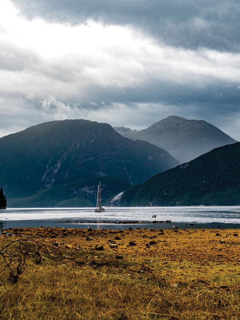 Passing Cloud, the 70-foot schooner anchored in a peaceful fjord within the Great Bear Rainforest of British Columbia