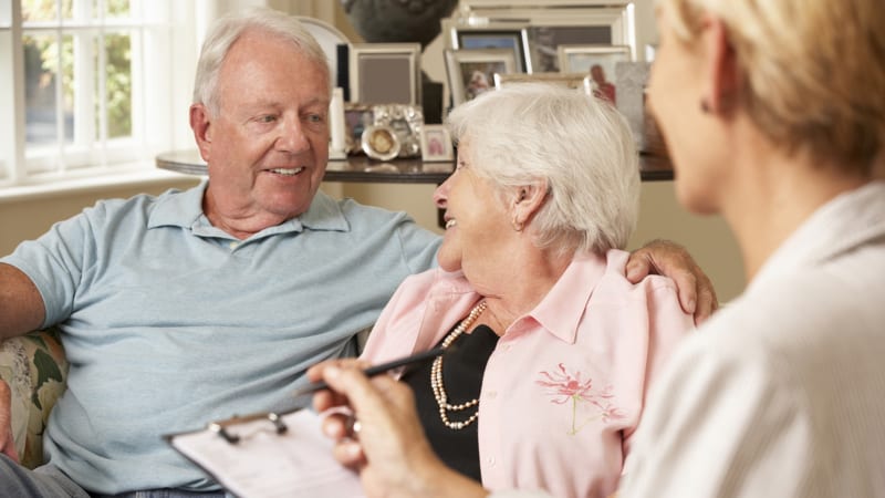 Retired Senior Couple Sitting On Sofa Talking To Financial Advisor