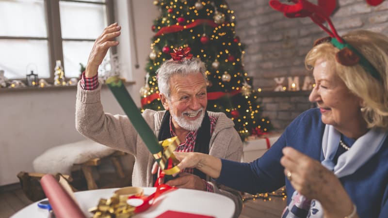 Senior couple wrapping Christmas presents to keep holiday cheer high and avoid getting stressed out