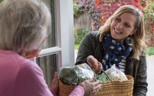 A woman volunteering with Naborforce brings an elderly local groceries Image