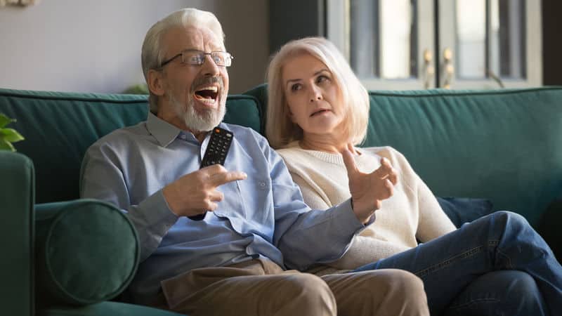 Angry father-in-law watching TV with his wife who looks like she regrets marrying him in the first place Image