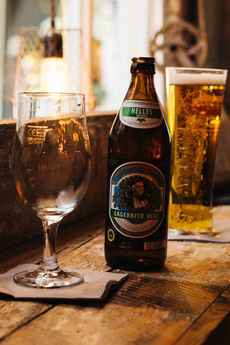 Helles beer bottle and stemmed beer glass with lager in the background