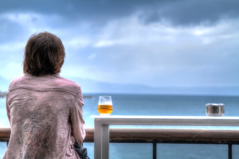 Woman gazing at gray sky and ocean while enjoying a beer