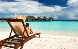 Woman on a tropical beach reading on a tablet. For Boomer expands in the digital world Image
