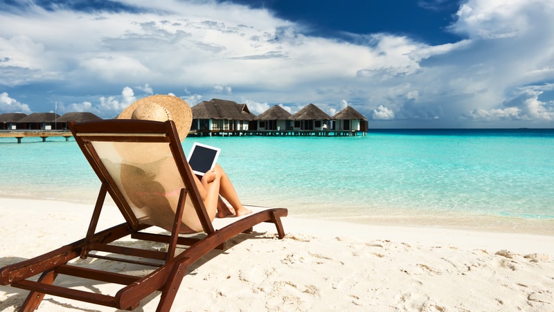 Woman on a tropical beach reading on a tablet. For Boomer expands in the digital world