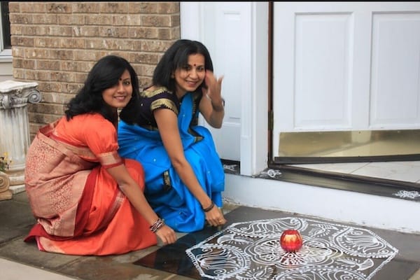 Two young Indian women in traditional saris on front porch with kolam