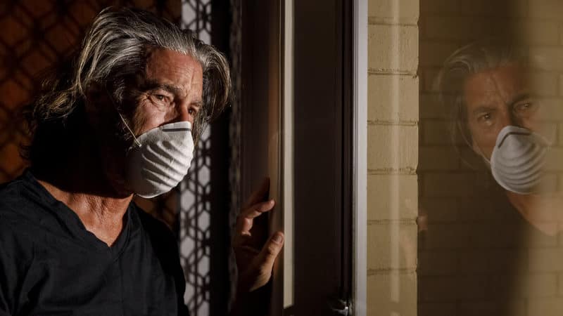 COVID mental health repercussions as man in mask peers sadly out the window. A picture of pandemic stress Image