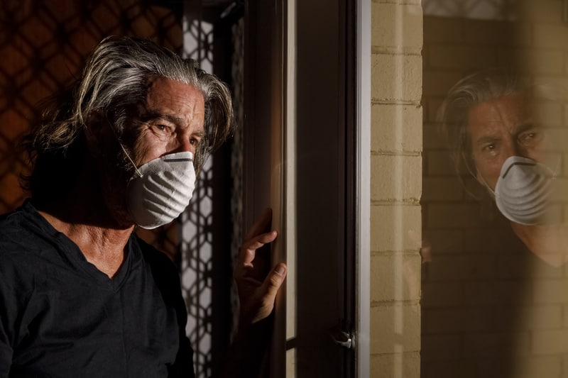 COVID mental health repercussions as man in mask peers sadly out the window. A picture of pandemic stress