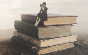 Surreal picture of a woman reading on top of a stack of old books. For Book recommendations for summertime reading Image