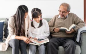 Multigenerational family - Asian mom, daughter, and granddad reading on family sofa, for 
