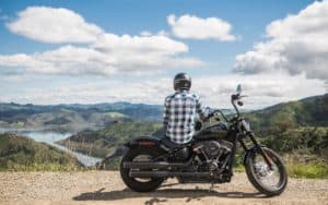 Motorcyclist sitting on motorcycle looking over lake and valley. For 5 Motorcycle Road Trip Tips Image