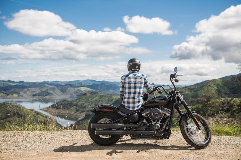 Motorcyclist sitting on motorcycle looking over lake and valley. For 5 Motorcycle Road Trip Tips