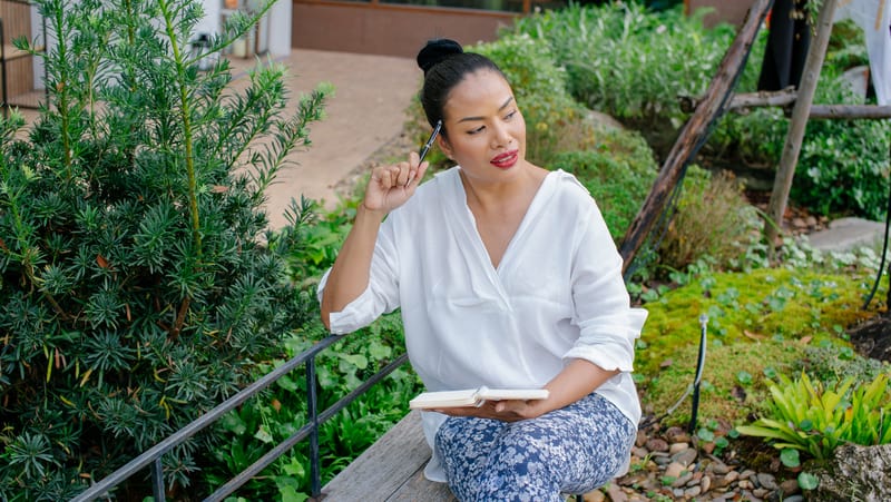 woman contemplating and journaling in a peaceful garden setting - for "starting again with journaling and action"