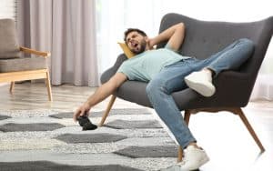 lazy young man lying on a love seat holding a video game controller. For article on A Baby Boomer’s Take on a Zoomer’s Future Image