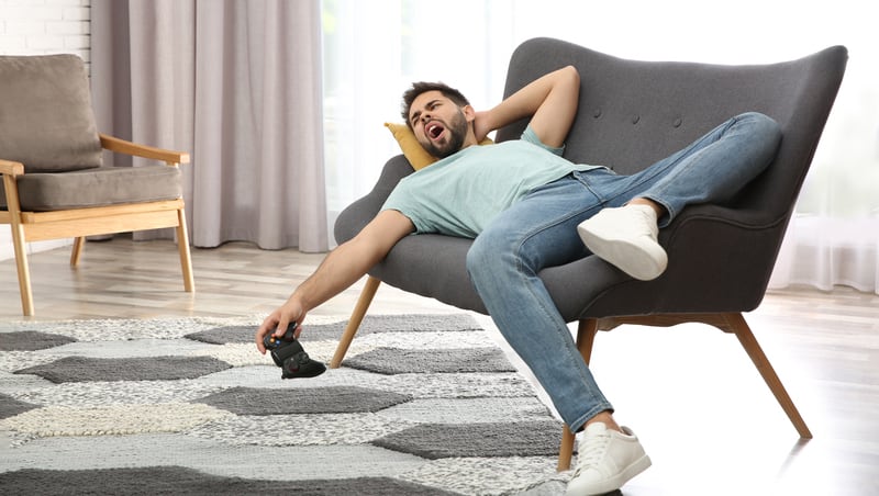 lazy young man lying on a love seat holding a video game controller. For article on A Baby Boomer’s Take on a Zoomer’s Future