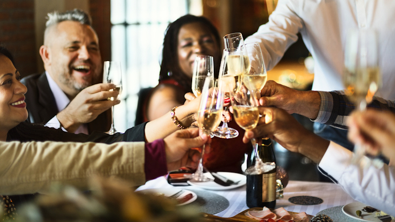 People celebrating with Champagne at a dinner party. Photo Rawpixelimages Dreamstime. For article on Taking Leftover Containers to a Dinner Party