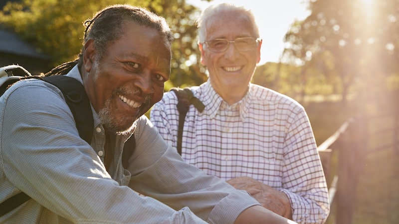 Two older men smiling, standing by a fence. For article on Should friend have reached out?