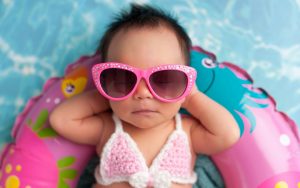Newborn baby girl wearing pink crocheted bikini top and sunglasses, on a pool float Photo Katrina Trninich Dreamstime. For article on 2021 baby-naming inspirations Image