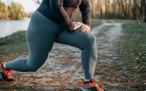 Someone overweight but stretching during exercise along a riverside fall pathway. For article, Can Fitness Counter Fatness? Image