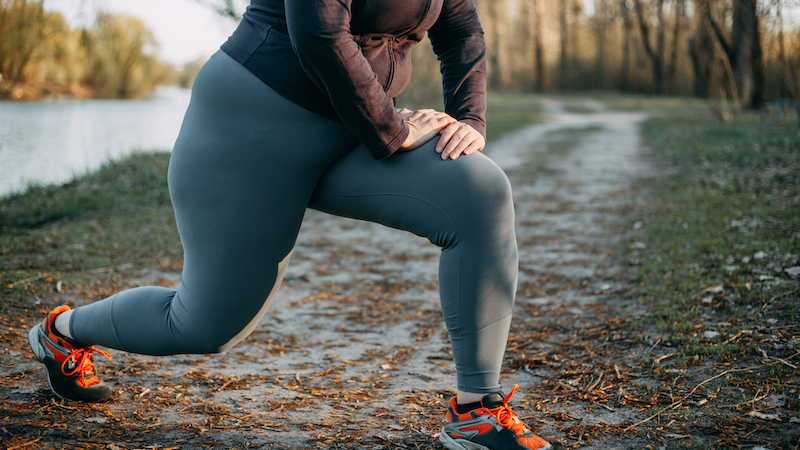 Someone overweight but stretching during exercise along a riverside fall pathway. For article, Can Fitness Counter Fatness?