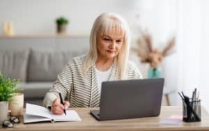 Woman at a laptop computer, with a notebook besides the laptop, possibly working on a puzzle Image