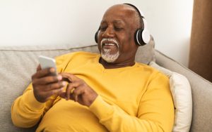 man at home with headphones and smartphone. photo by Milkos Dreamstime. For article on best podcasts for baby boomers. Image