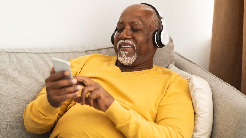 man at home with headphones and smartphone. photo by Milkos Dreamstime. For article on best podcasts for baby boomers. Image
