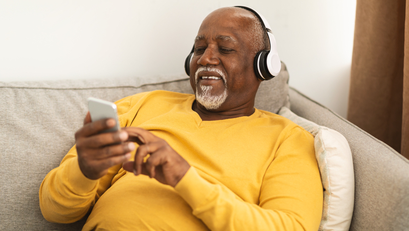 man at home with headphones and smartphone. photo by Milkos Dreamstime. For article on best podcasts for baby boomers.