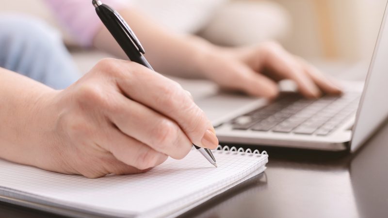 woman at a laptop playing a puzzle or otherwise making notes in a notebook on the side Image