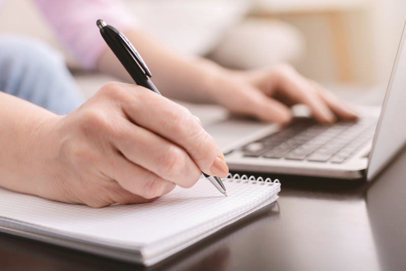 woman at a laptop playing a puzzle or otherwise making notes in a notebook on the side