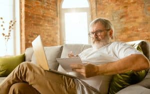 Man sitting on sofa with paper and laptop, possibly doing a puzzle. Image by volodymyr melnyk dreamstime Image