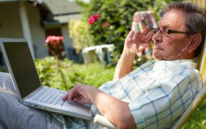 man outside on a laptop, possibly working on a puzzle. Photo by Nyul Dreamstime Image