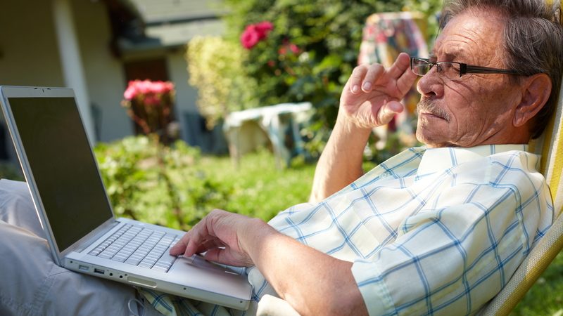 man outside on a laptop, possibly working on a puzzle. Photo by Nyul Dreamstime Image