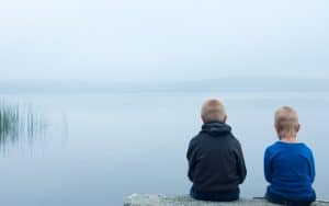 two sad boys sitting on a rock in front of a foggy lake Photo by Oksanabratanova Dreamstime. For article on helping grieving grandchildren Image