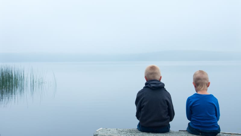 two sad boys sitting on a rock in front of a foggy lake Photo by Oksanabratanova Dreamstime. For article on helping grieving grandchildren
