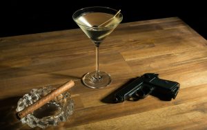 A cocktail, cigar, and gun on a table. Photo by Oliver Nowak Dreamstime. For article, The Chi-Chi Chowchilla cocktail was inspired by a kidnapping of a busload of children. The story and recipe appear in 'Mixology and Murders.' Image