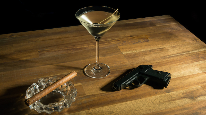 A cocktail, cigar, and gun on a table. Photo by Oliver Nowak Dreamstime. For article, The Chi-Chi Chowchilla cocktail was inspired by a kidnapping of a busload of children. The story and recipe appear in 'Mixology and Murders.'