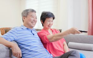 couple watching TV on their sofa, using the remote and smiling. Photo by Shao-chun Wang Dreamstime. For article, 31 perfectly paired romantic double feature movies, with a touch of romance and of LOL. Watch them or just get a laugh out of their couplings. Image