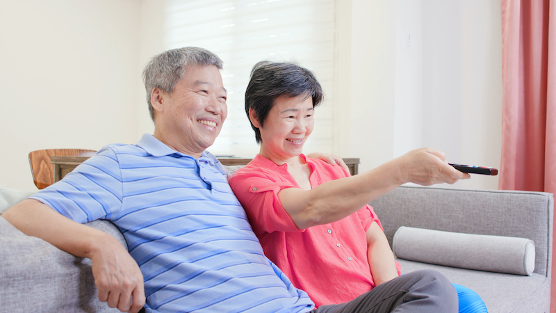 couple watching TV on their sofa, using the remote and smiling. Photo by Shao-chun Wang Dreamstime. For article, 31 perfectly paired romantic double feature movies, with a touch of romance and of LOL. Watch them or just get a laugh out of their couplings.