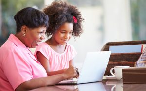 A grandmother and granddaughter on a laptop, possibly doing puzzles or browsing the internet. Photo by Monkey Business Images Dreamstime Image