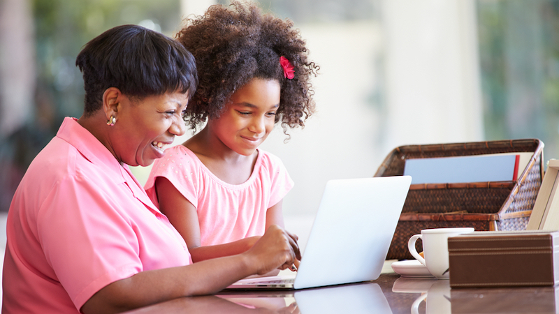 A grandmother and granddaughter on a laptop, possibly doing puzzles or browsing the internet. Photo by Monkey Business Images Dreamstime