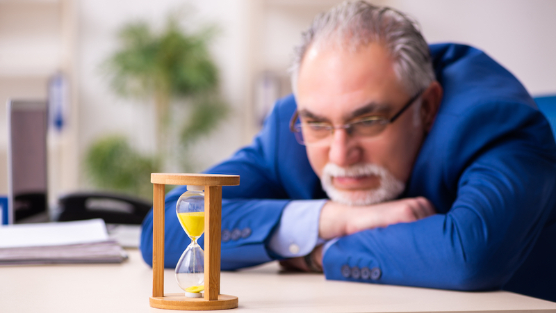 office worker looking at hourglass photo by Elnur Dreamstime. For article, Humorist Greg Schwem extolls the virtues (and hints at hidden downsides) of an idea whose time has come: the one-day work week.