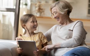 grandmother granddaughter on a tablet, maybe playing a puzzle, laughing. Photo by Fizkes Dreamstime Image