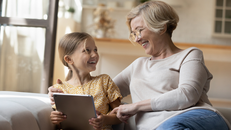 grandmother granddaughter on a tablet, maybe playing a puzzle, laughing. Photo by Fizkes Dreamstime