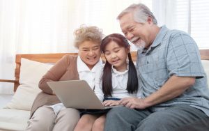 grandparents granddaughter looking together at a laptop, possibly doing a puzzle, sitting on a sofa. Photo by Champaiporn Kitina Dreamstime Image
