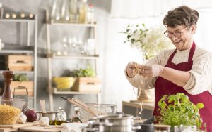 happy woman cooking pasta and vegetables in her kitchen. Photo by Katarzyna Bialasiewicz Dreamstime. For article on responses to uppity vegetarians and vegans Image