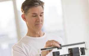 man on scale photo by Tmcphotos Dreamstime. For article on Maintaining Your Weight to Feel Great Image