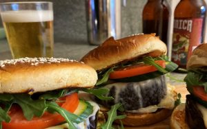 Roasted eggplant burgers served with craft beer for National Beer Day. The trick to successful meatless burgers is to vary the textures so the bite satisfies. A roasted vegetable makes a meatless burger superior to a pre-made protein patty, then the Sweet and Smoky Glaze is the cherry on top. Image