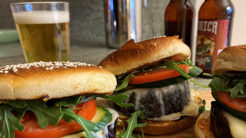 Roasted eggplant burgers served with craft beer for National Beer Day. The trick to successful meatless burgers is to vary the textures so the bite satisfies. A roasted vegetable makes a meatless burger superior to a pre-made protein patty, then the Sweet and Smoky Glaze is the cherry on top.